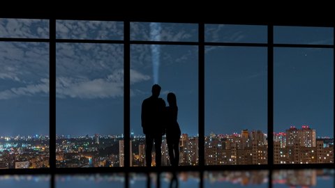 The man and woman stand near the windows on the night city background. time lapse