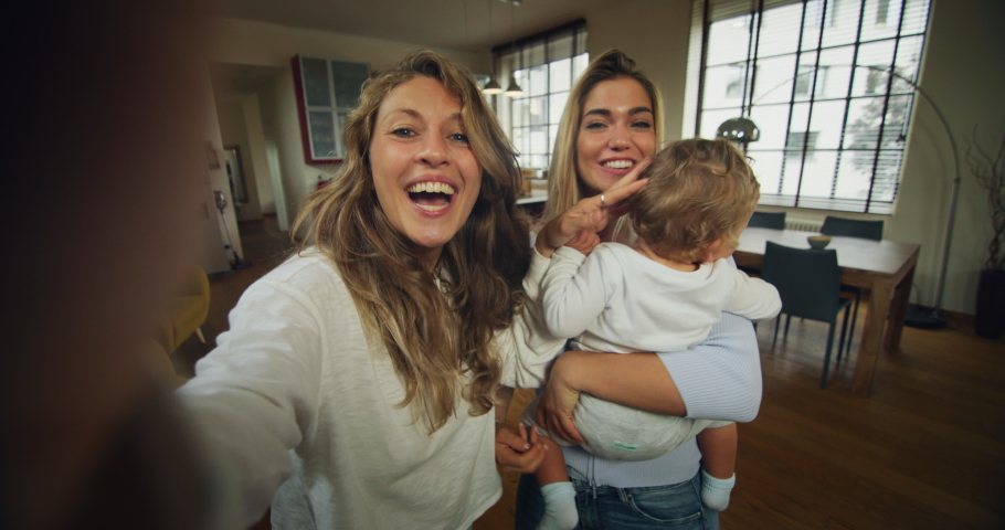 Authentic shot of young happy homosexual female gay family with son toddler baby boy is making a selfie or video call to friends or relatives in a living room at home. Royalty-Free Stock Footage #1060180319
