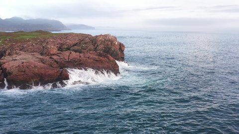 Cinematic low altitude aerial orbit of rocks, ocean crashing and seabirds flying in Newfoundland Canada.