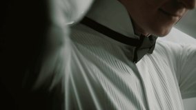 Groom in with a beard stands by the window in a white shirt and examines a bow tie. - Powered by Shutterstock - Get 15% off with code: PIKWIZARD15