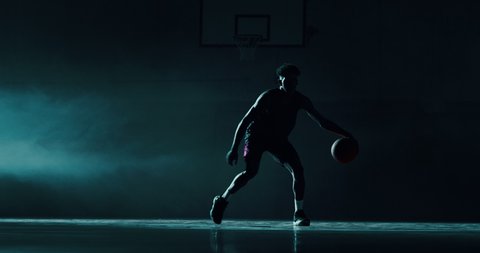 Cinematic slow motion shot of an young african professional male player is practicing a basketball work out in a gym.