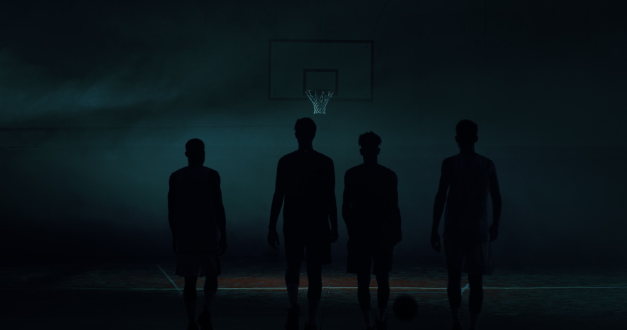 Cinematic slow motion back view shot of young professional male players are walking towards a basket before to start practicing a basketball work out in a gym.