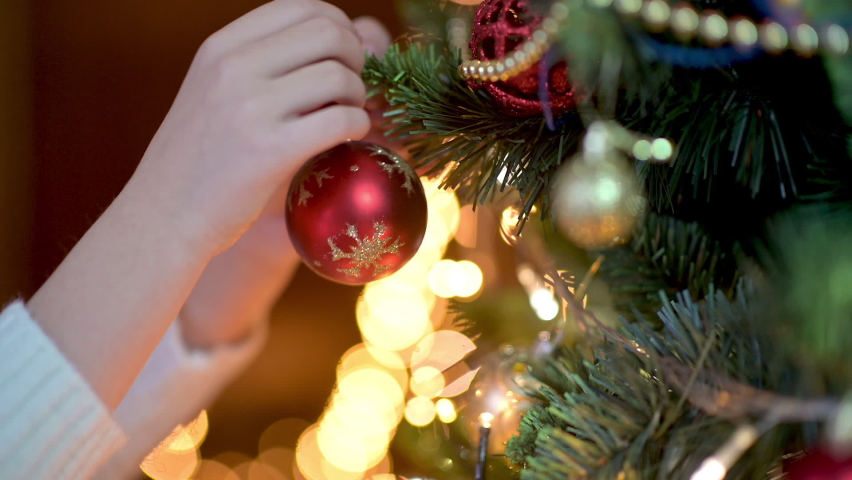 Close-up of kid's hands decorating Christmas tree with balls on the background of bright festive lights. children decorating a Christmas tree. | Shutterstock HD Video #1060182365