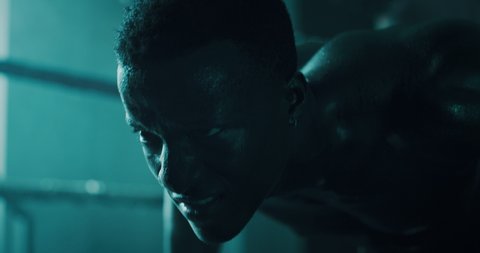 Cinematic slow motion shot of a professional young muscular shirtless african man is practicing shadow boxing work out in a gym with ring. 