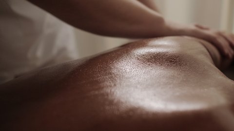 Extreme closeup manual therapist hands massaging female back with oil during relaxing or revitalizing procedure at Thai beauty spa salon woman client lying on couch enjoying body and skin care