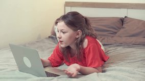 A brunette girl lies on a white bed and communicates online. Communication with relatives at a distance using video communication.