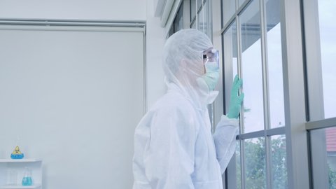 Asian man scientist is wearing Personal Protective Equipment (PPE) looked at the window while in laboratory. Disease quarantine Impact Coronavirus