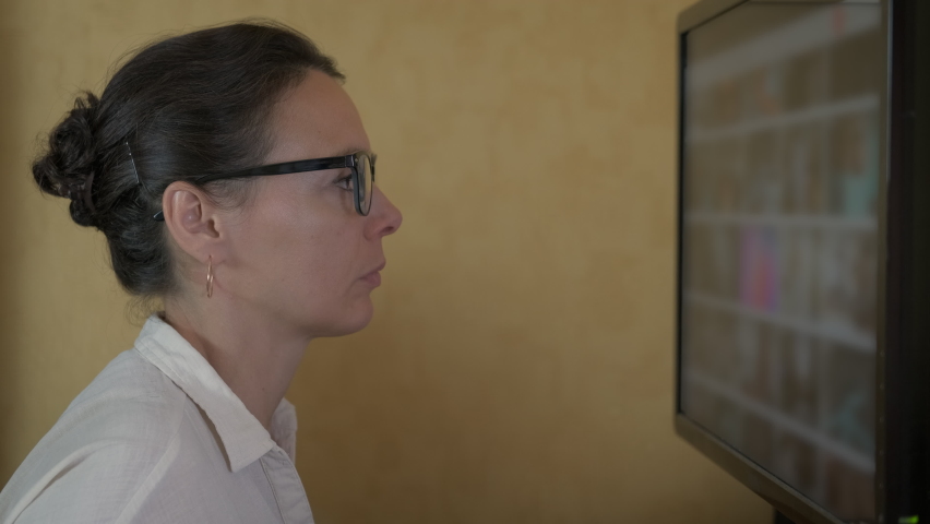 Woman watch the video screen. A nice woman in glasses look at the screen with video in the room. | Shutterstock HD Video #1060189451