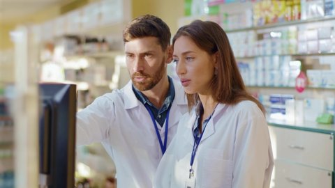 Two medical workers man and woman cooperating in apothecary. Professional adult pharmacist coaching female intern. Collaboration. Medication, healthcare, drugs.