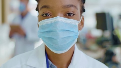 Closeup portrait of professional apothecarist pharmacy expert african american woman wearing respiratory mask working in drugstore. Blurred background.