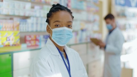 Portrait of intelligent female pharmacist professional woman with braids wearing protective antiviral mask looking at camera. Apothecarist. Mixed race. Profession.