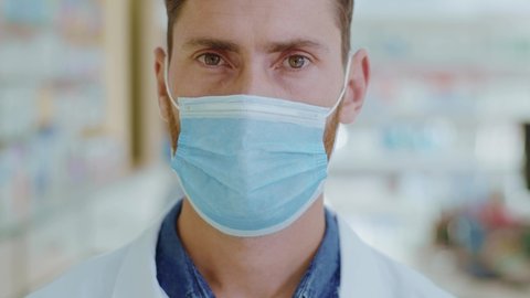Portrait of male adult pharmacist consultant with respiratory mask. Apothecarist man with female colleague working during quarantine coronavirus pandemic. Close-up.