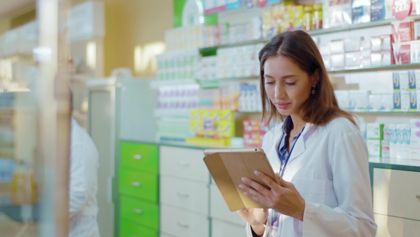 Pharmacy female consultant using digital tablet for learning drugs searching medication details online coworking in professional drugstore. People and occupation. Medical sector. Royalty-Free Stock Footage #1060193996