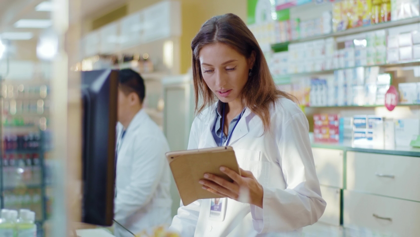 Pharmacy female consultant using digital tablet for learning drugs searching medication details online coworking in professional drugstore. People and occupation. Medical sector. Royalty-Free Stock Footage #1060193996