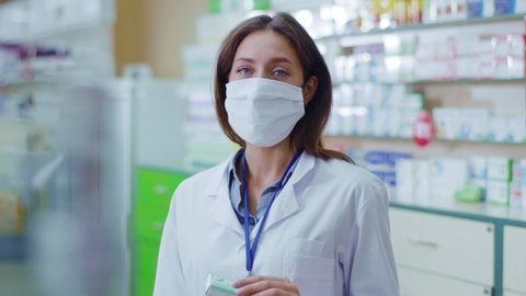 Young woman pharmacy worker inspecting drug packs with computer database learning wearing protective face mask against coronavirus. Pandemic. Apothecary. Healthcare.
