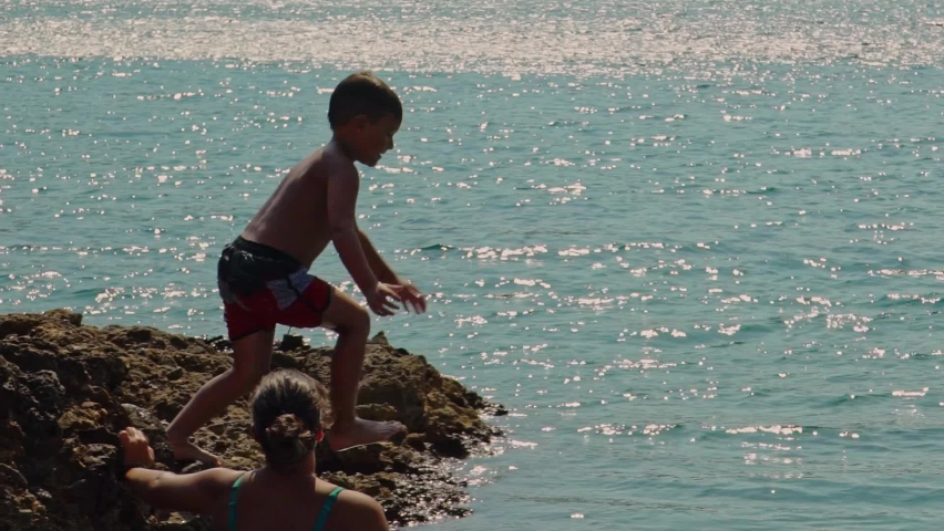 Caucasian boy jumps from rocks to sea for the first time, while his mother watching, slow motion