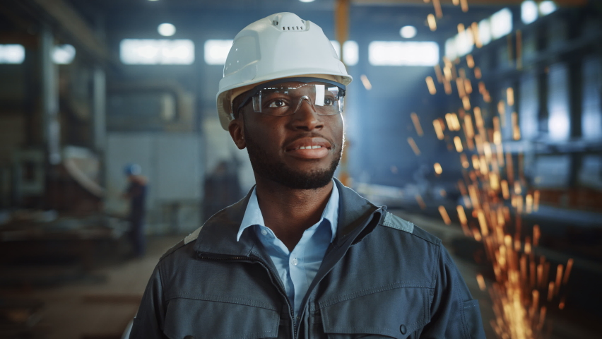 Happy Professional Heavy Industry Engineer/Worker Wearing Uniform, Glasses and Hard Hat in a Steel Factory. Smiling African American Industrial Specialist Standing in a Metal Construction Manufacture. | Shutterstock HD Video #1060203749