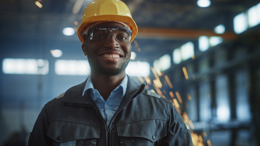 Happy Professional Heavy Industry Engineer/Worker Wearing Uniform, Glasses and Hard Hat in a Steel Factory. Smiling African American Industrial Specialist Standing in a Metal Construction Manufacture. | Shutterstock HD Video #1060203752