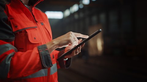Close Up on Hands of a Professional Female Heavy Industry Engineer Wearing Safety Uniform and Using Tablet Computer. Industrial Specialist Standing in a Metal Construction Manufacture.