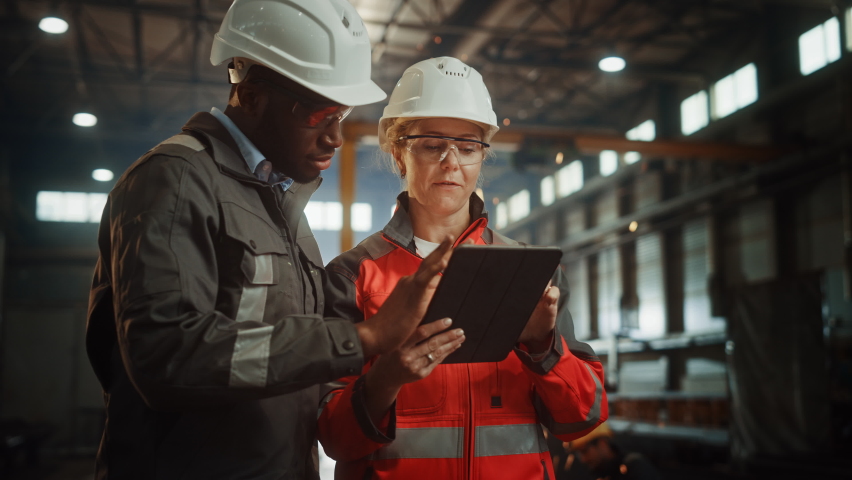 Two Heavy Industry Engineers Stand in Steel Metal Manufacturing Factory, Use Digital Tablet Computer and Have a Discussion. Black African American Industrial Specialist Talk to Female Technician. | Shutterstock HD Video #1060203905