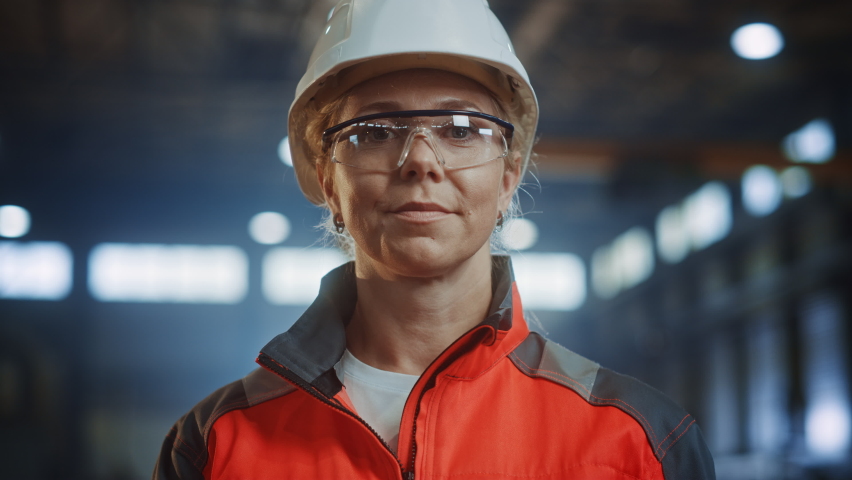 Portrait of a Professional Heavy Industry Engineer/Worker Wearing Uniform, Glasses and Hard Hat in a Steel Factory. Beautiful Female Industrial Specialist Standing in Metal Construction Facility. | Shutterstock HD Video #1060203929