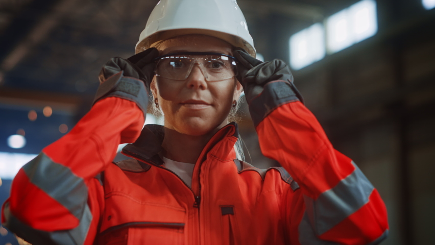 Portrait of a Professional Heavy Industry Engineer/Worker Wearing Uniform, Glasses and Hard Hat in a Steel Factory. Beautiful Female Industrial Specialist Standing in Metal Construction Facility. | Shutterstock HD Video #1060203932