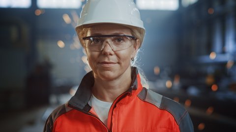 Portrait of a Professional Heavy Industry Engineer/Worker Wearing Uniform, Glasses and Hard Hat in a Steel Factory. Beautiful Female Industrial Specialist Standing in Metal Construction Facility.