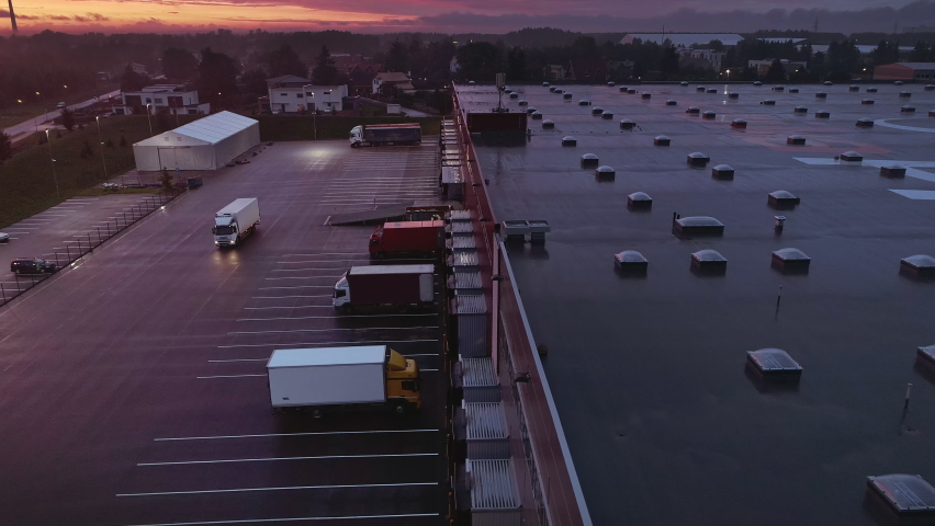 Aerial Moving Footage with Multiple Loading Stations with Lorry Trucks at an Industrial Warehouse of Logistics Building. Evening Twilight Sunset with Light Clouds and Pink Hue. Royalty-Free Stock Footage #1060204025