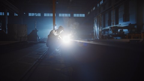 Heavy Industry Engineering Factory Interior with Industrial Worker Using a Welding Machine and Working on a Metal Tube. Contractor in Safety Uniform and Hard Hat Manufacturing Metal Structures.