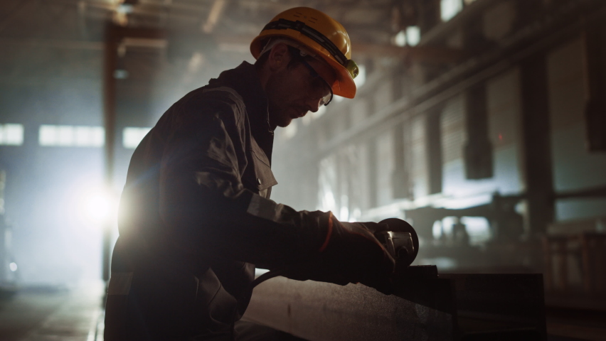 Heavy Industry Engineering Factory Interior with Industrial Worker Using Angle Grinder and Cutting a Metal Tube. Contractor in Safety Uniform and Hard Hat Manufacturing Metal Structures. Royalty-Free Stock Footage #1060204070