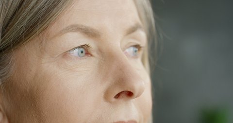 Close up of face of senior Caucasian blonde businesswoman taking off glasses, looking at side and thinking. Indoor. Tired middle-aged serious woman.