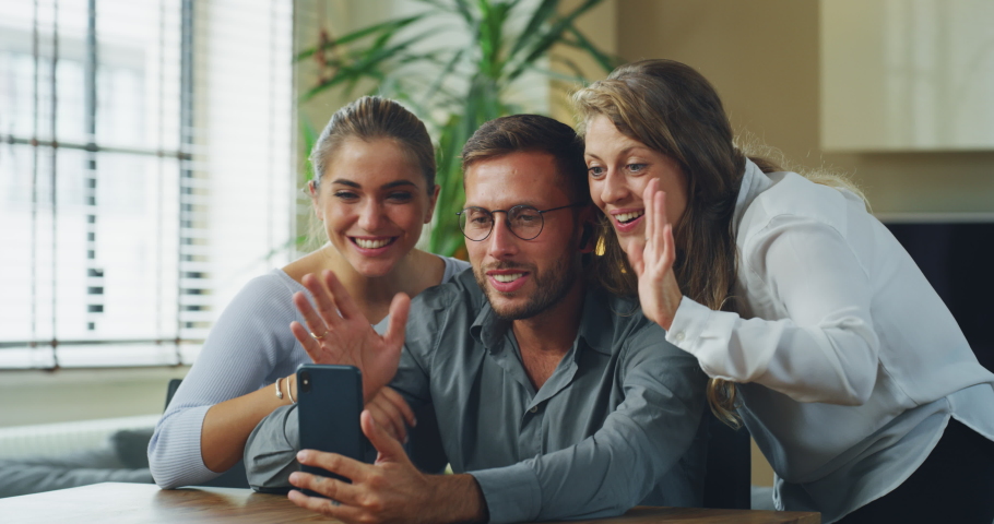 Authentic shot of young happy college friends are making a selfie or video call to relatives or friends with smartphone in a living room at home. | Shutterstock HD Video #1060209764