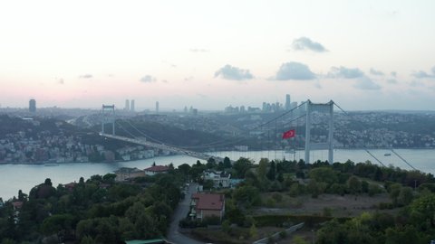 Turkish Flag Waving in Wind in front of Istanbul Bosphorus Bridge and City Skyline at Beautiful Sunset, Establishing Aerial slide right