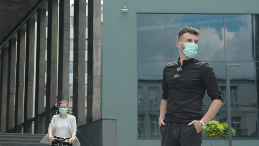The girl comes to the meeting on an electric scooter. Young people in medical masks on their faces. Meeting of two young happy people on the street in the middle of the city.
