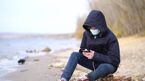 teen playing online video games sitting on autumn empty beach during pandemic coronavirus season.