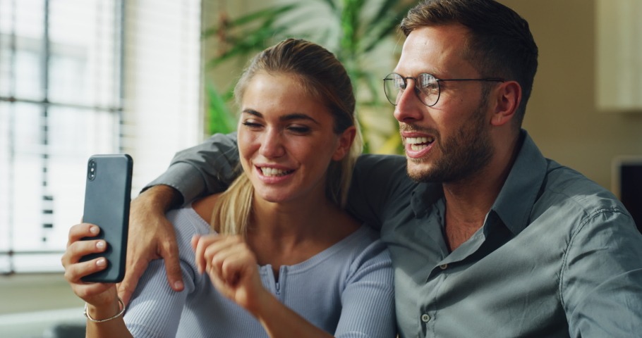 Authentic shot of happy smiling married couple is making video technology call to friends or family with smartphone from home and showing an ultrasound to announce their future child birth. | Shutterstock HD Video #1060215974
