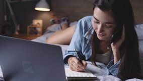 A young woman lies on her be with a laptop  and works from home online