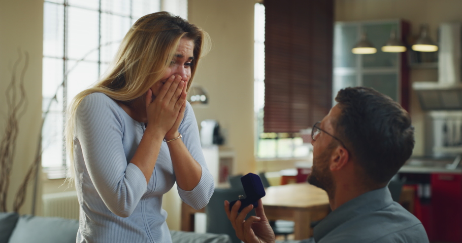Authentic shot of young handsome man is making a surprise proposal of marriage to his beloved woman in living room at home. The woman is accepting emotionally and giving a hug full of love | Shutterstock HD Video #1060217639