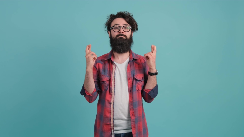 Concentrated young man that keeps fingers crossed and making a wish, isolated over turquoise background. | Shutterstock HD Video #1060221641