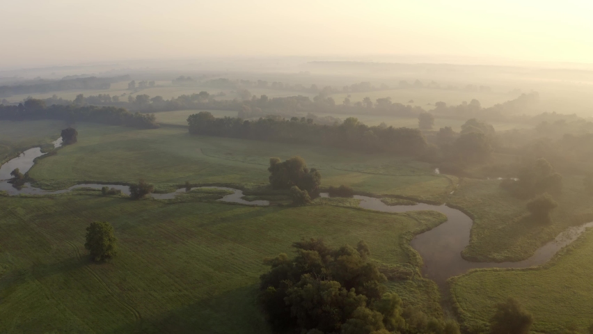 River arm with meanders from aerial view at sunrise. Summer nature scenery illuminated by morning sun. Green riparian forest and floodplain meadows near Moravia river, Slovakia.