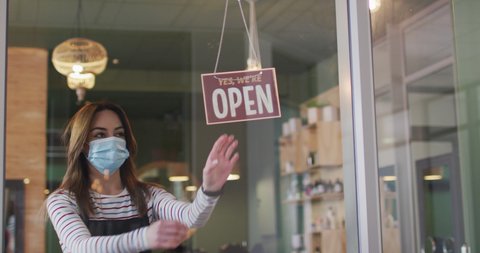 Caucasian female hairdresser working in hair salon wearing face mask, switching sign to Sorry, We Are Closed, slow motion. Health and hygiene in workplace during Coronavirus Covid 19 pandemic.