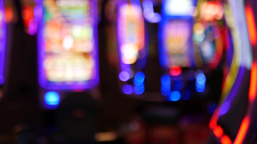 Defocused slot machines glow in casino on fabulous Las Vegas Strip, USA. Blurred gambling jackpot slots in hotel near Fremont street. Illuminated neon fruit machine for risk money playing and betting. | Shutterstock HD Video #1060223921