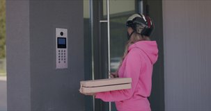 Delivery man waiting for customer at entrance door of modern house. Female courier wearing in protective medical mask holding boxes of pizza. 4k raw slow motion footage 50 fps
