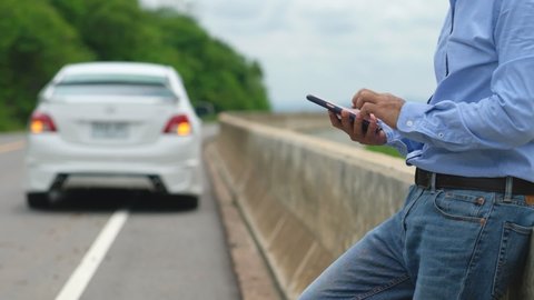 A man is using his smartphone and social media to get help because his car is broken. And park beside the road