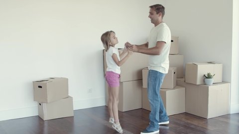 Active dad and daughter celebrating moving, having fun and dancing in their new apartment. Full length. Moving into new house concept
