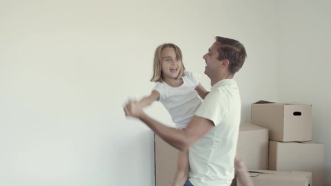 Joyful dad holding daughter in arms and dancing, celebrating moving, having fun in their new apartment. Moving into new house concept