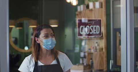 Caucasian female hairdresser working in hair salon wearing face mask, switching sign to Yes, We Are Open, slow motion. Health and hygiene in workplace during Coronavirus Covid 19 pandemic.