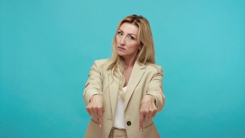 Here and now. Self confident bossy woman in business suit pointing fingers seriously looking at camera, strict leader controlling work process. Indoor studio shot isolated on blue background