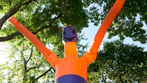 Blowing Tube Man in advertising. Waving Flailing Arms Wacky Tube Man on a Background of Green's Trees in the Park. Funny Orange Inflatable Figure Dancing in the Wind. Air Generic Advertising Sign