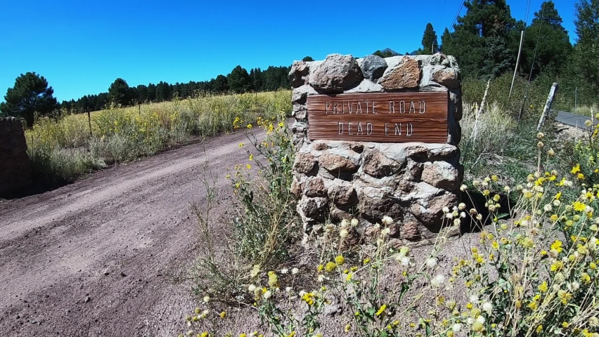 A private country road is marked with a stone pillar and wooden sign, Flagstaff, Arizona. Copy space